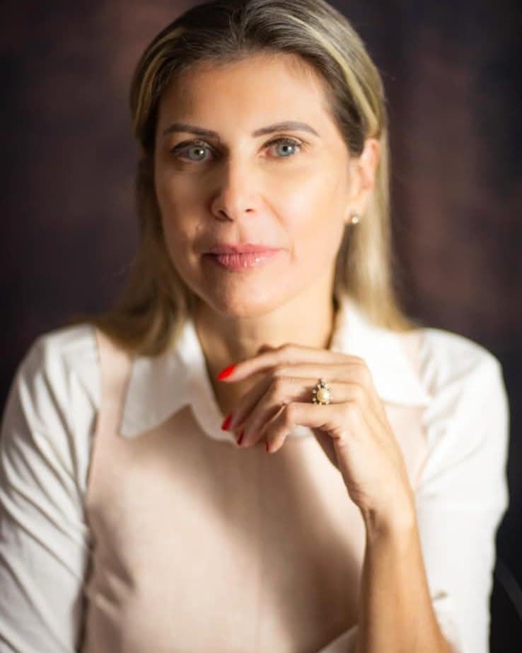 Dra. Christianne Feldmann (Chris), especialista em longevidade da pele, em retrato profissional com blusa clara sobre fundo escuro